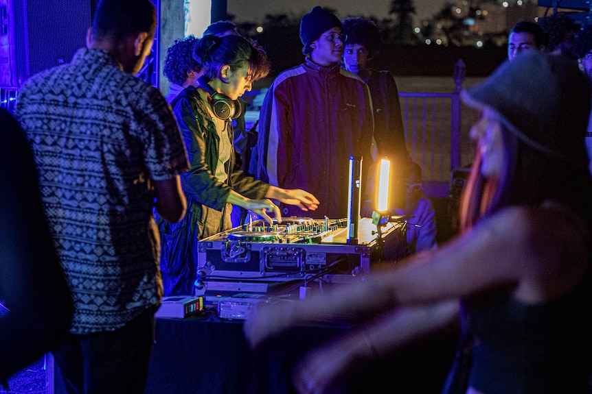 Egyptian DJ A7ba-L-Jelly plays music on a DJ console as people dance in the foreground