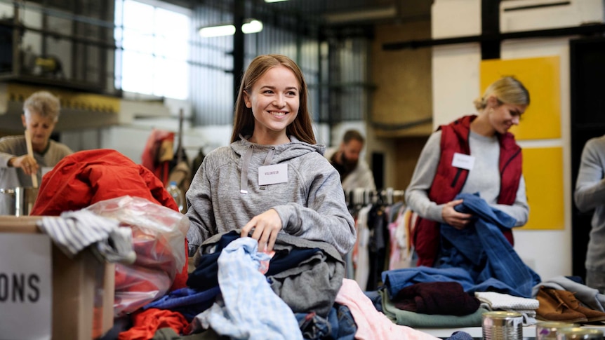 A young woman wearing a 'volunteer' name tag sorts clothes in a donation centre.