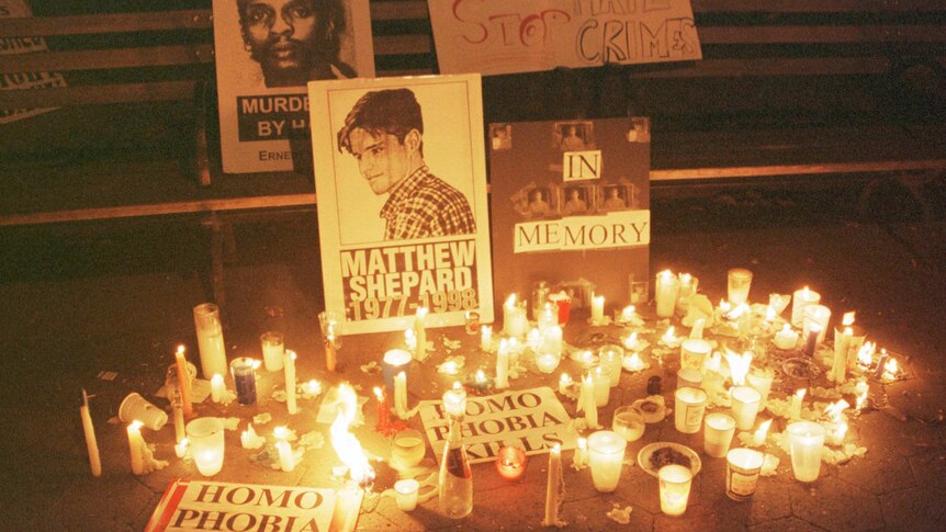 Lit candles surround posters with slogans including "stop hate crimes" and "homophobia kills".