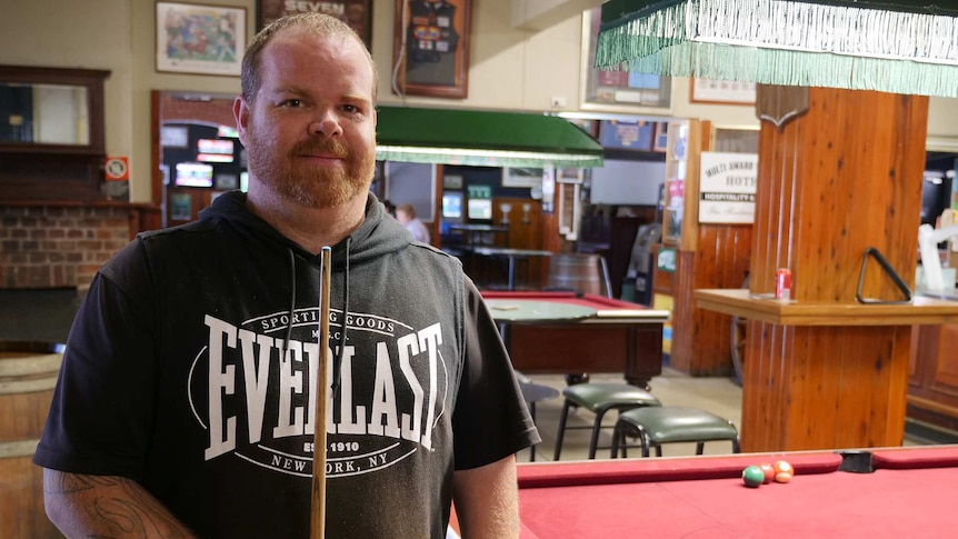 A man in a black shirt stands in a pub at a pool table.