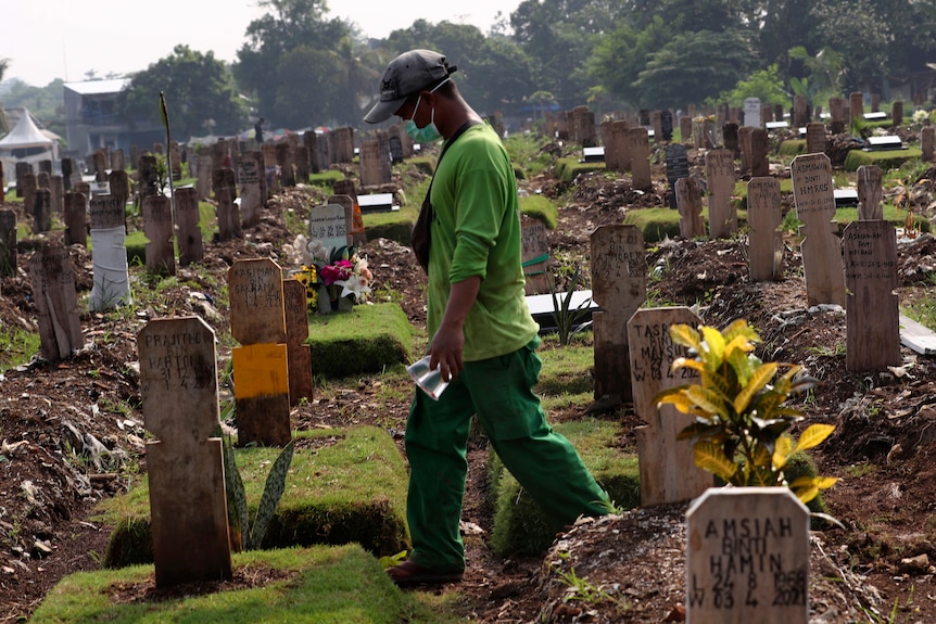 Seorang pekerja berjalan melalui kuburan di Jakarta di antara batu nisan korban COVID19