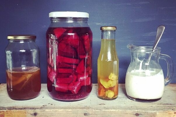 Jars of food waste that are being turned into fermented drink tonics sit on a wooden board.