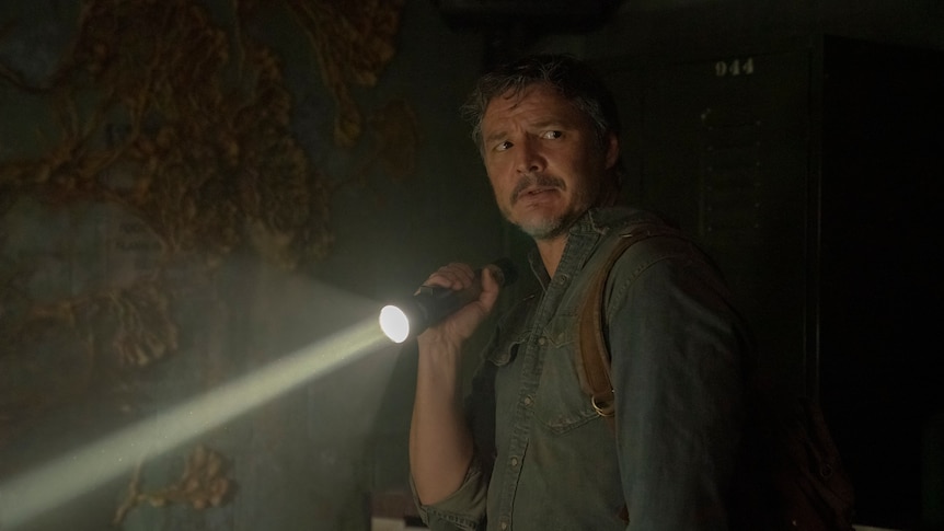 A man holds a torch and looks pensive, behind him on the wall grows yellow funghi.