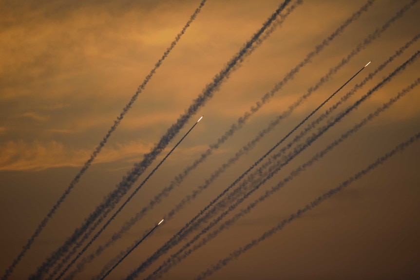 Bright flames and dark smoke from rockets and projectiles can be seen criss-crossing the orange sky.