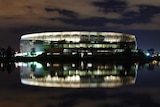 Perth Stadium lit up at night with a reflection in the Swan River.