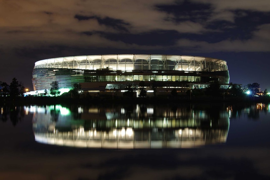 Perth Stadium lit up at night with a reflection in the Swan River.