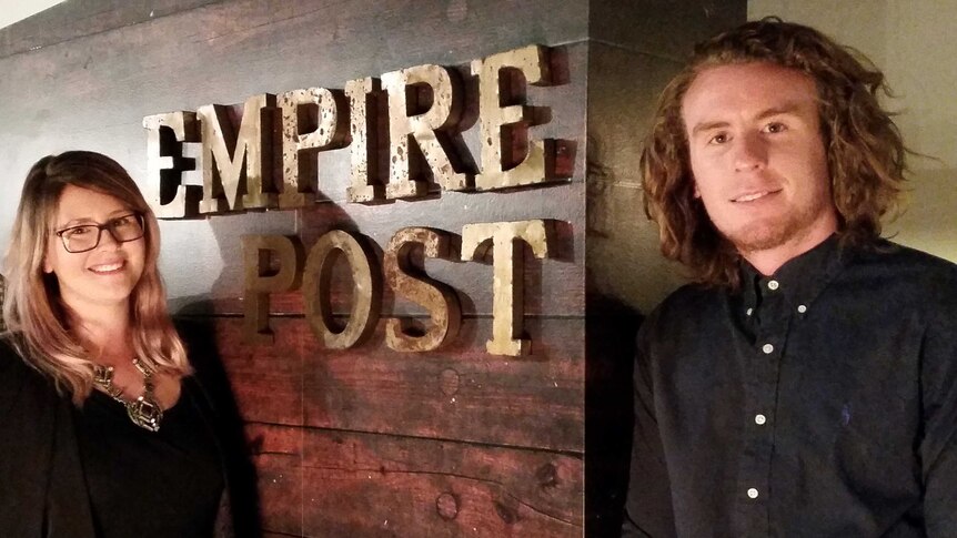 Empire Post managing director Nicole Manns and her business partner Digby Hogan in front of a corporate sign.