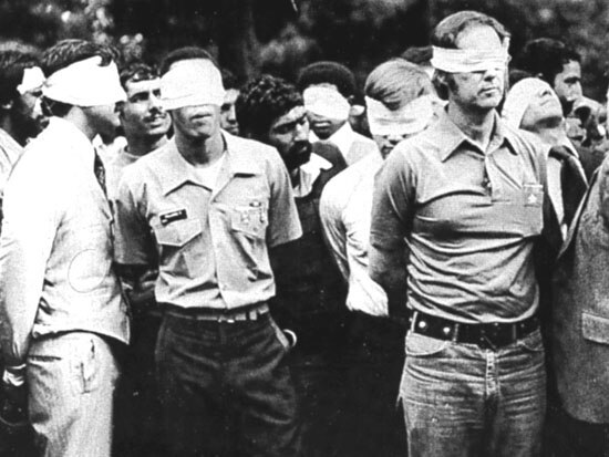 A black and white photo of several men who are blindfolded and their hands tied behind their backs.