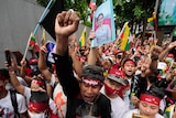 一群举着旗帜和昂山素季画像的缅甸抗议者，其中一人举起了拳头
