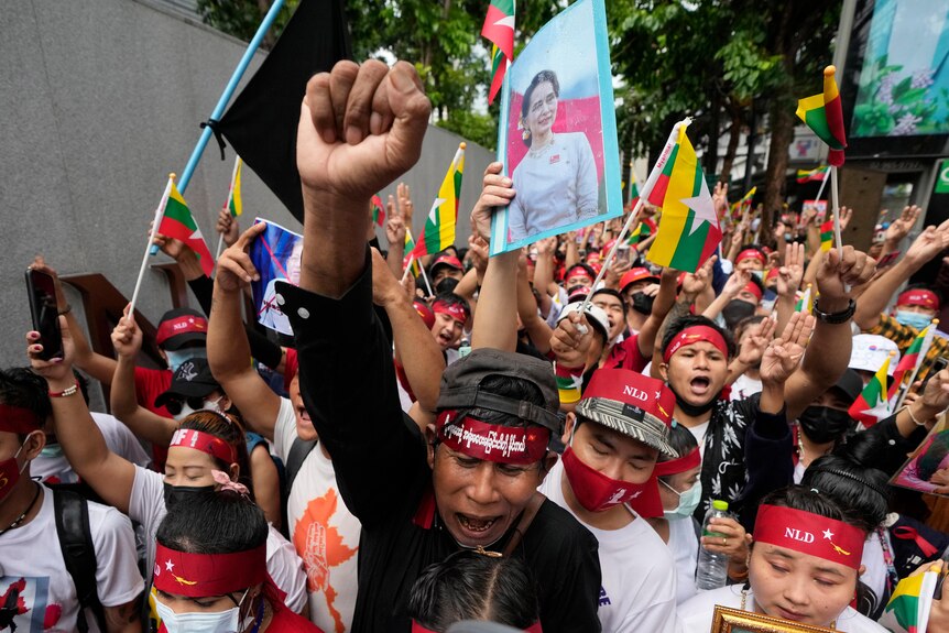 A group of Myanmar protesters with flags and portraits of Aung San Suu Kyi, one with a raised fist
