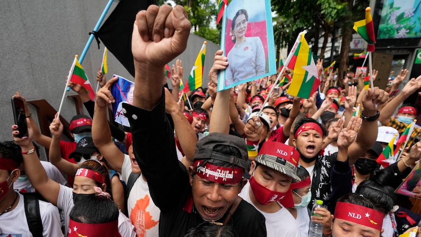 A group of Myanmar protesters with flags and portraits of Aung San Suu Kyi, one with a raised fist