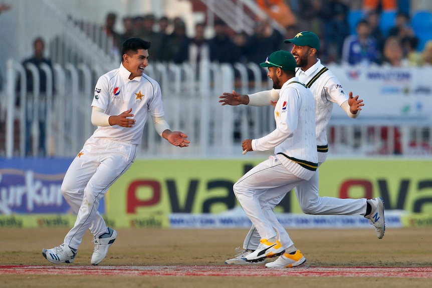 A bowler turns to face his teammates who run in to congratulate him on his Test hat-trick.