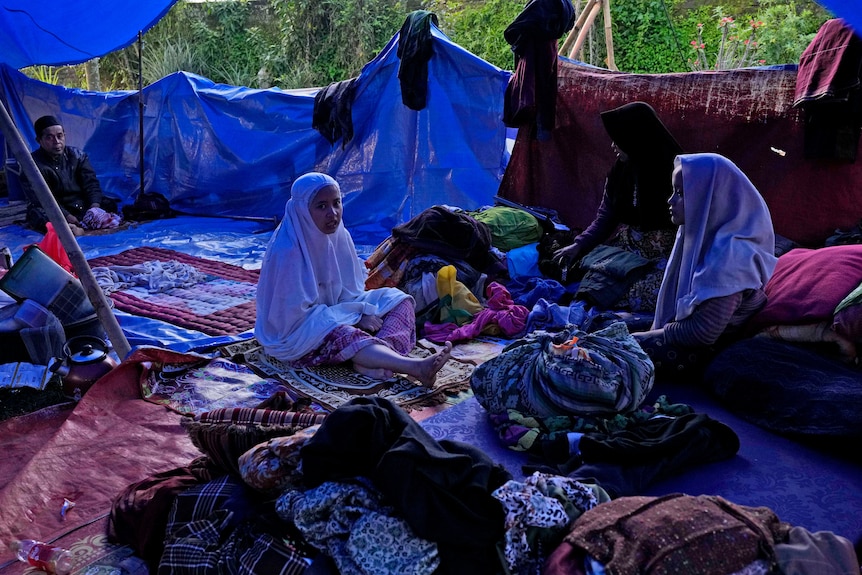 Earthquake survivors sit under a makeshift tent at their temporary shelter.