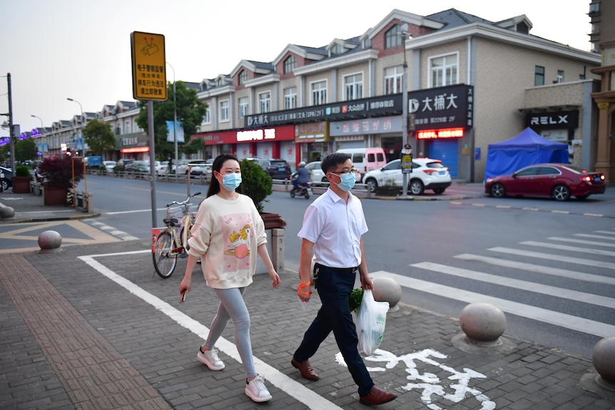 Two people Chinese people with masks walk down a Shanghai street