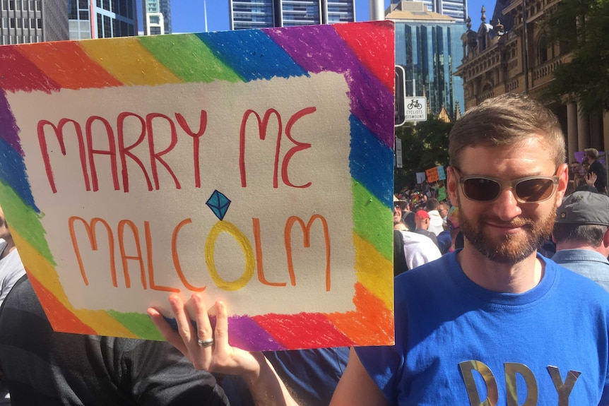 Man with palcard reading 'Marry me Malcolm'