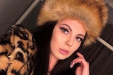 a woman posing with a fur hat and coat on, she has dark hair and eyes