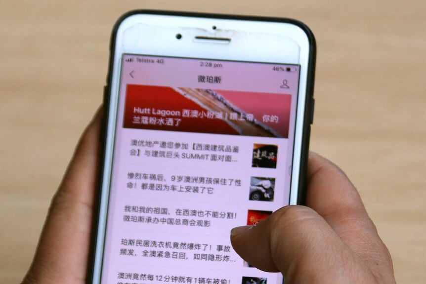 A man holds a mobile phone with Chinese writing on it.