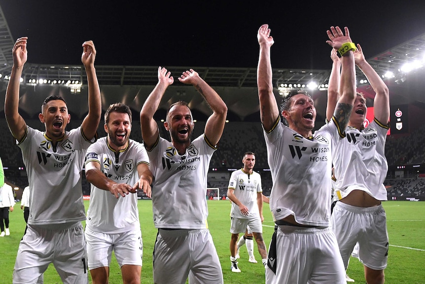 Players wearing white jerseys wave their hands towards a crowd.