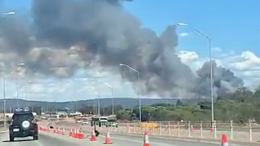 A bushfire burns off in the distance and cars slow through roadworks