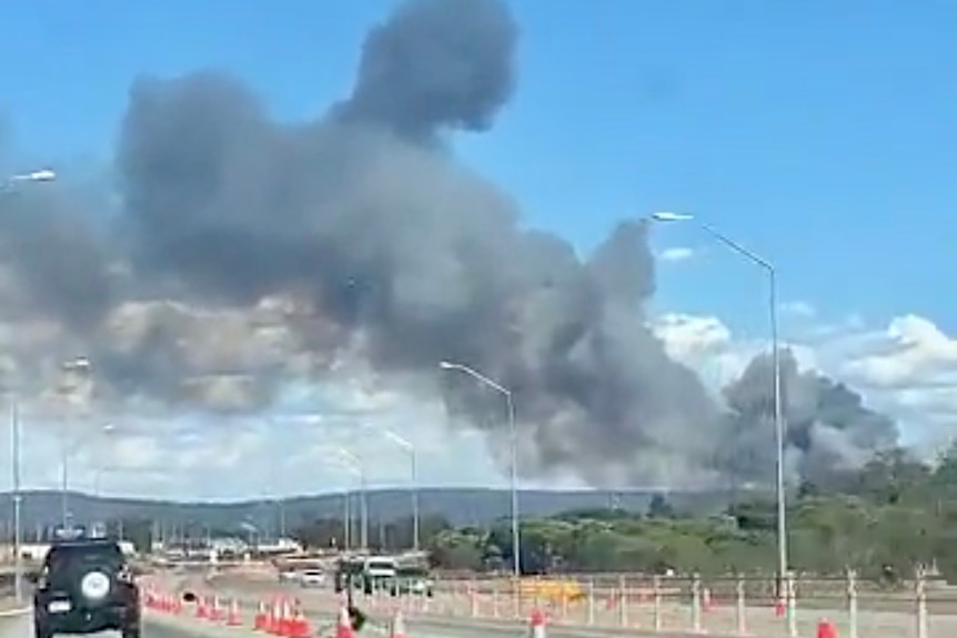 A bushfire burns off in the distance and cars slow through roadworks