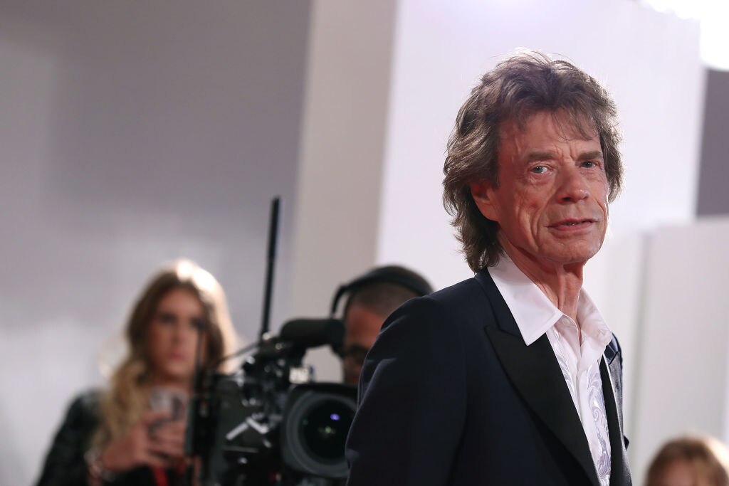 An older man looks thoughtfully at the camera as a video camera can be seen in the background.