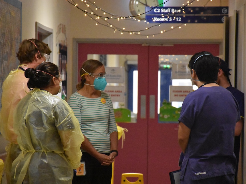 Men and women wearing masks and ppe stand in a hospital corridor and talk.