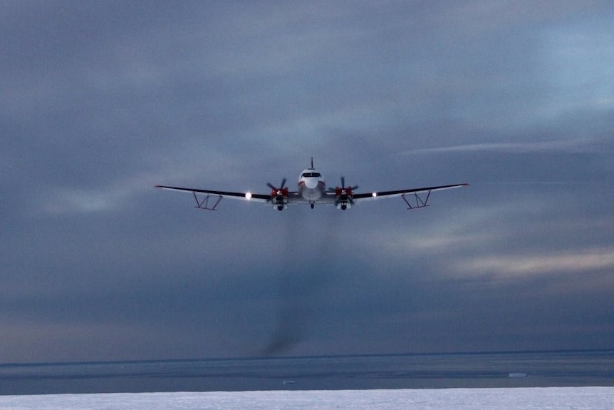 A plane with a slight trail of smoke flies over the surface of Antarctica