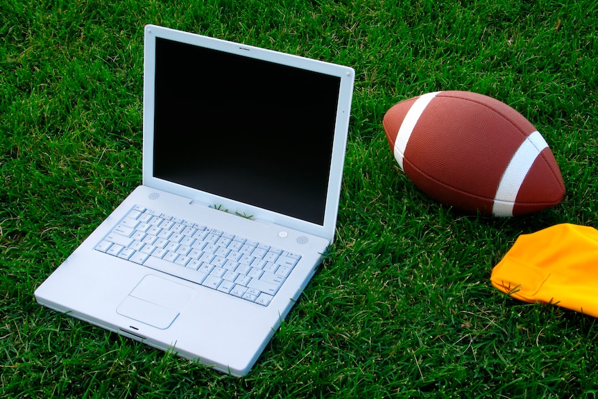 A white laptop lays open on green grass next to a football