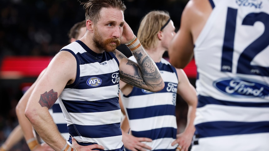 Zach Tuohy holds his hand to his head and looks disappointed while standing with Geelong teammates