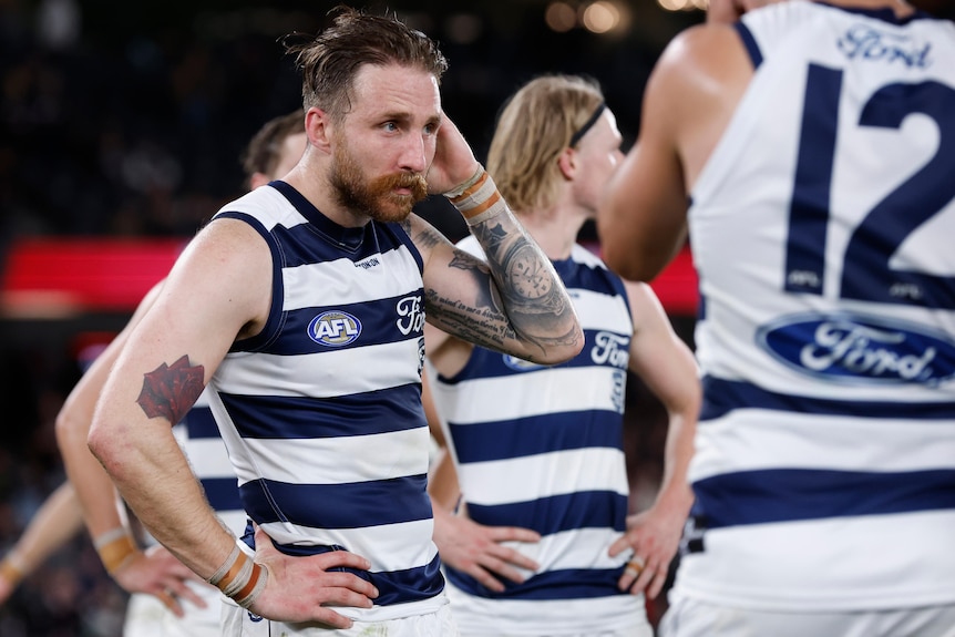 Zach Tuohy holds his hand to his head and looks disappointed while standing with Geelong teammates