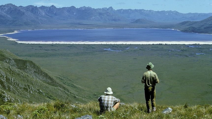 Two hikers look out at a lake, with mountains in the background.