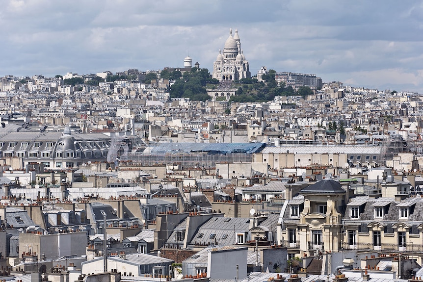 You view a dense cityscape of Paris as buildings go up a hill to a classical church on its top.