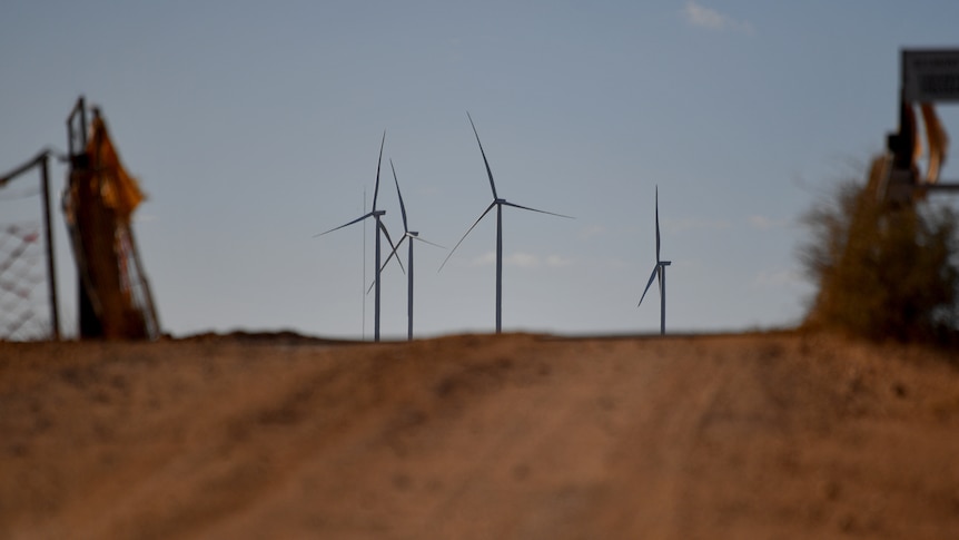 Brown dusty road with wind turbines in the distance