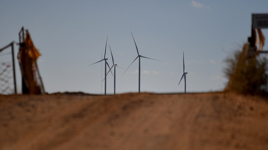 Brown dusty road with wind turbines in distance