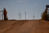 Brown dusty road with wind turbines in distance
