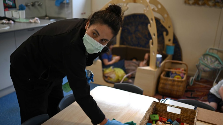 A woman cleaning a child care room wearing a mask