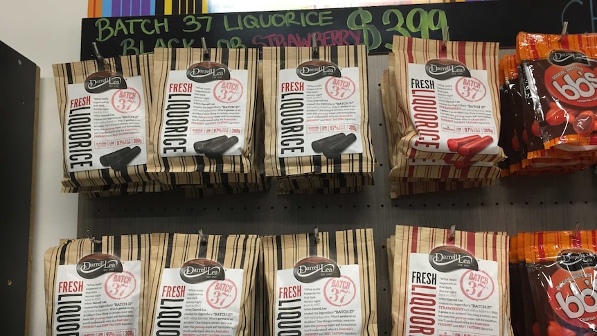 Two rows of Darrell Lea Batch 37 licorice hanging on hooks on a wall with a partially obscured price above hand written above