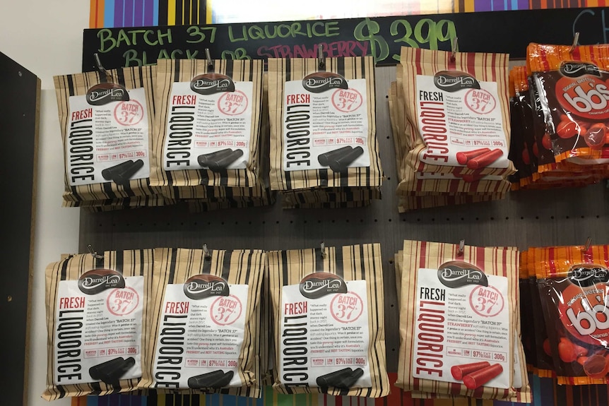 Two rows of Darrell Lea Batch 37 licorice hanging on hooks on a wall with a partially obscured price above hand written above