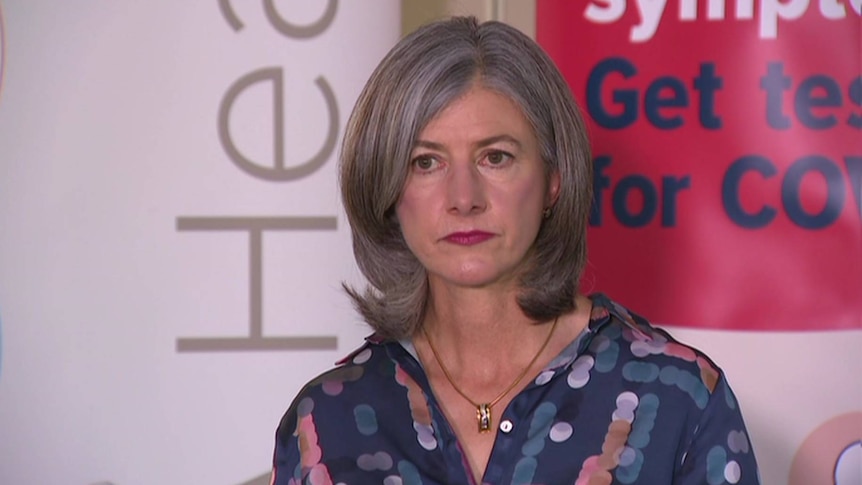 A woman with grey hair and a blue shirt standing in front of a banner