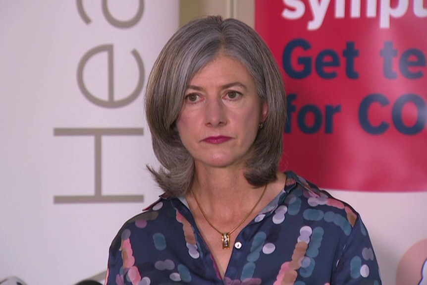 A woman with grey hair and a blue shirt standing in front of a banner