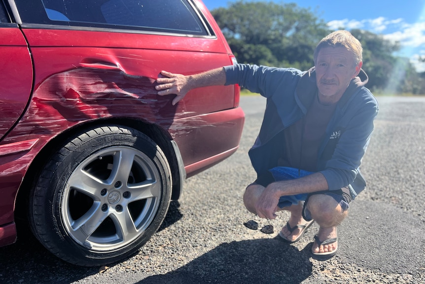 A man inspects the damage to his car after is was rammed by another vehicle.