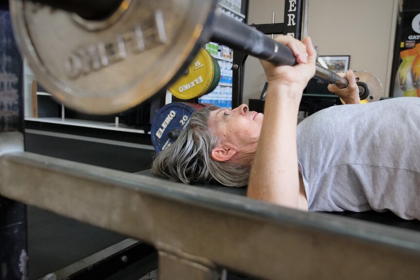 Close-up of woman with grey hair doing a bench press.