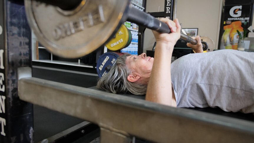Close-up of woman with grey hair doing a bench press.