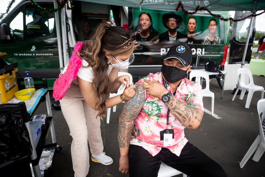 A man rolls up his sleeve and gets a jab.  