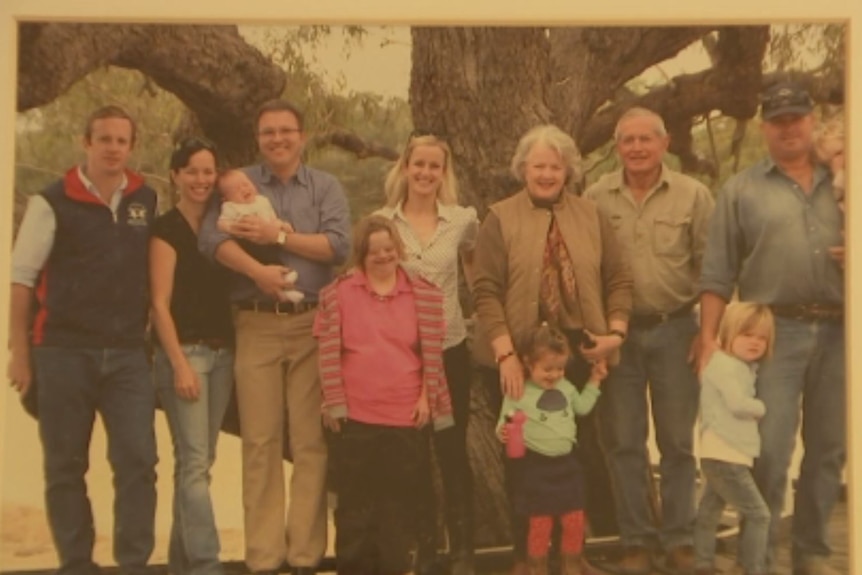 A sepia-toned, old photograph of 11 people standing under a tree