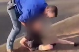 Man in jeans and blue shirt holds a teenage boy on the ground, his face blurred.