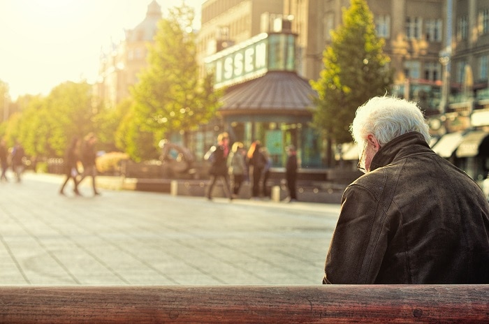 An old man sits alone on a bench in the middle of a city square