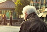 An old man sits alone on a bench in the middle of a city square