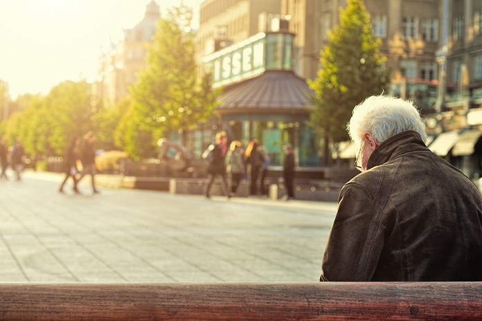 An old man sits alone on a bench in the middle of a city square