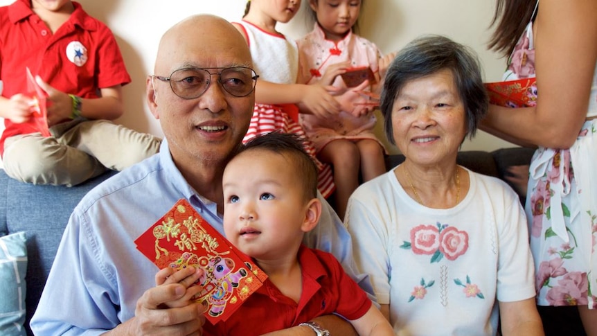 A man, woman and baby sit and hold red cards given to them on the Lunar New Year.